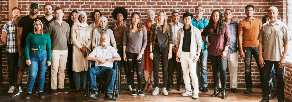 Group of people of diverse ages standing against a brick wall