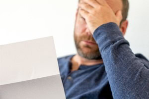 Picture of a middle aged man sitting down and looking upset reading a letter