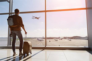 man-standing-with-luggage-looking-out-at-window-in-airport