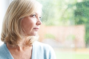 50-year-old woman looking out windown on rainy day