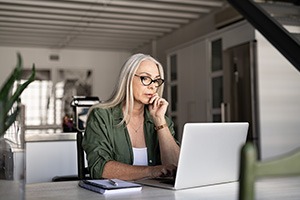 Middle aged woman looking worried researching on computer