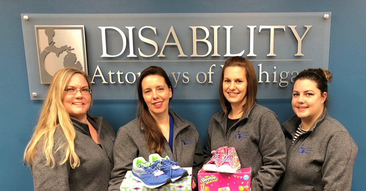 Disability Attorneys of Michigan staff and lawyer holding donations of shoes