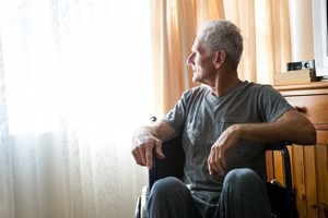 Man looking out window sitting in wheelchair in nursing home