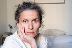 Middle aged woman sitting on bed, looking upset