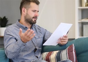 Picture of a man sitting on th couch looking upset reading a letter