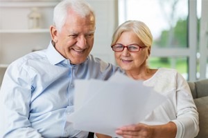 Picture of an elderly retired couple sitting on the couch looking happy reading papers