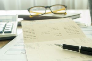 Picture of calculator, checkbook pen, book and reading glasses on a desk