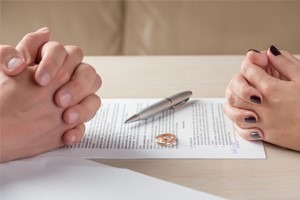 man and woman signing divorce papers, wedding rings off